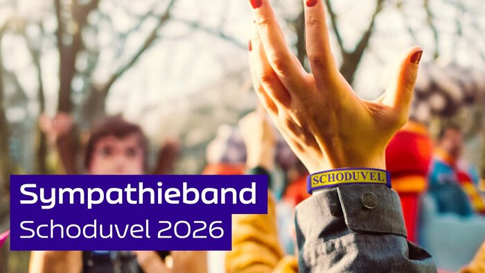 Im Vordergrund eine Hand mit einem lila-gelben Armband, auf dem Schoduvel steht. Im Hintergrund feiernde Menschen und ein Karnevals-Umzugswagen