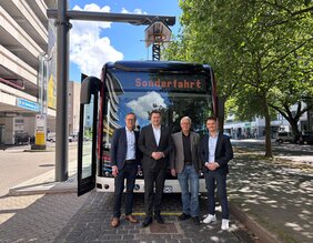 Vier Männer in Anzügen stehen vor einem Bus. In dessen Zielfilm steht Sonderfahrt